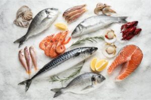 An arrangement of various types of seafood, including shrimp, salmon, and lobster, lying on ice with decorative lemons.