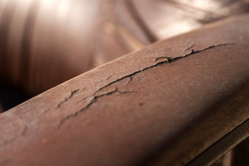 A close-up of a brown leather chair. The chair is sitting in sunlight, and cracks are on its arm.
