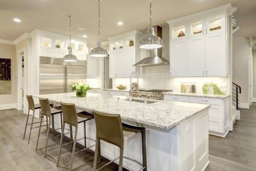 A modern kitchen with a large island, granite counters, white cabinetry, stainless steel appliances, and pendant lights.