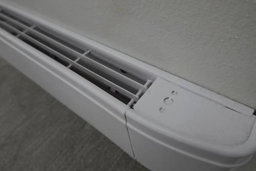 Closeup of a white electric baseboard heater attached to a wall, with the vents positioned at the top.