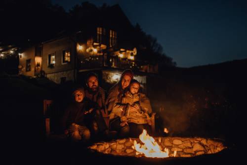 A family of four gathered around their backyard fire pit. The sky is dark and they're bundled together on chairs.