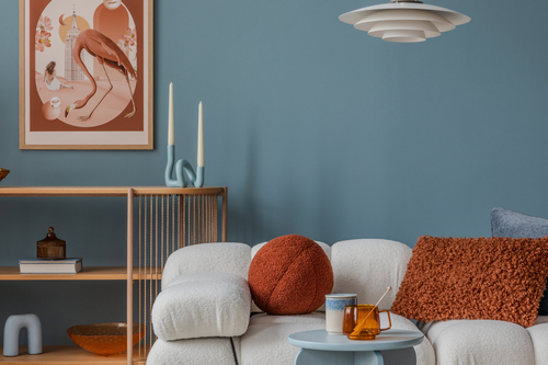 A contemporary living room space with a blue accent wall, cream-colored couch, and orange textured throw pillows.