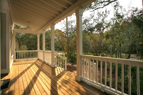 A large porch is undecorated. The awning is tall and the wood is clean, and past the porch there are a lot of trees.