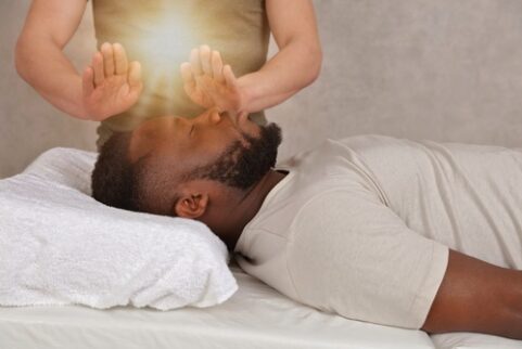 A man lying down on a table with his eyes closed while a person above them holds their hands over his face.